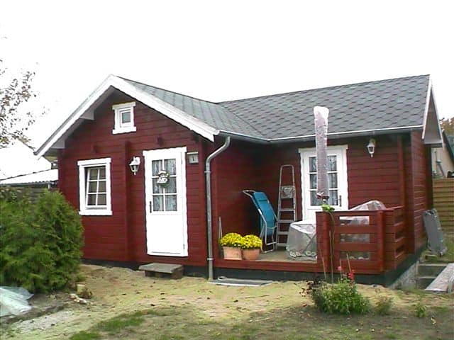 Ein kleines Ferienhaus mit weißen Verzierungen und einer Veranda mit Stuhl und Whirlpool.