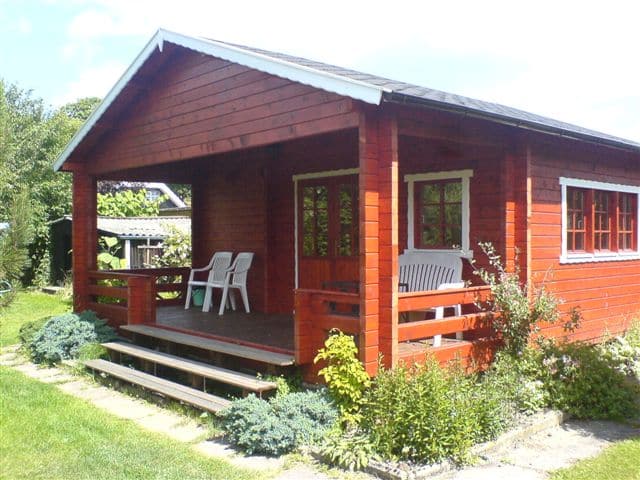 Eine rote Holzhütte mit einer Veranda mit zwei Stühlen und einer Bank, umgeben von einer grünen Wiese in Jütland.