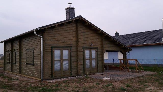 Ein einstöckiges Ferienhaus aus Holz mit Satteldach und mehreren Glastüren, gelegen auf einem Grundstück mit einer kleinen Veranda an der Seite.