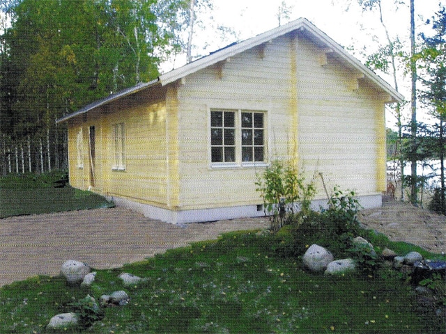 Ein einstöckiges, gelbes Ferienhaus mit weißen Verzierungen, umgeben von Grün und einem mit Steinen gesäumten Weg.